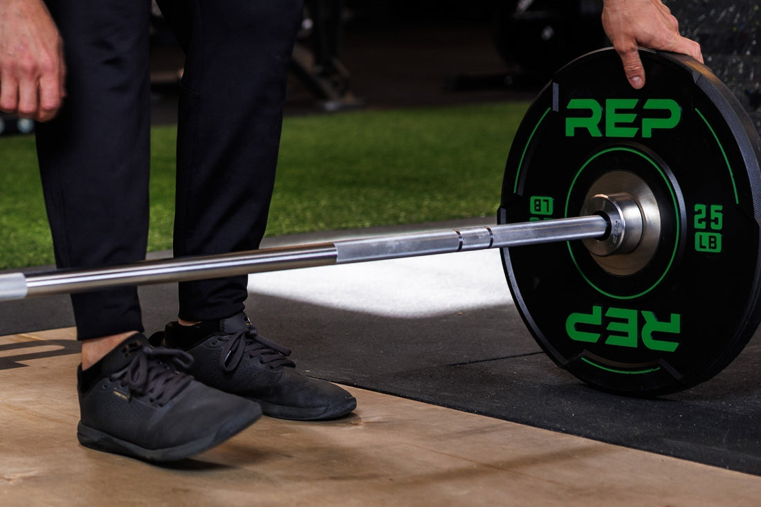 A person checks their 25lb REP bumper plates on a barbell