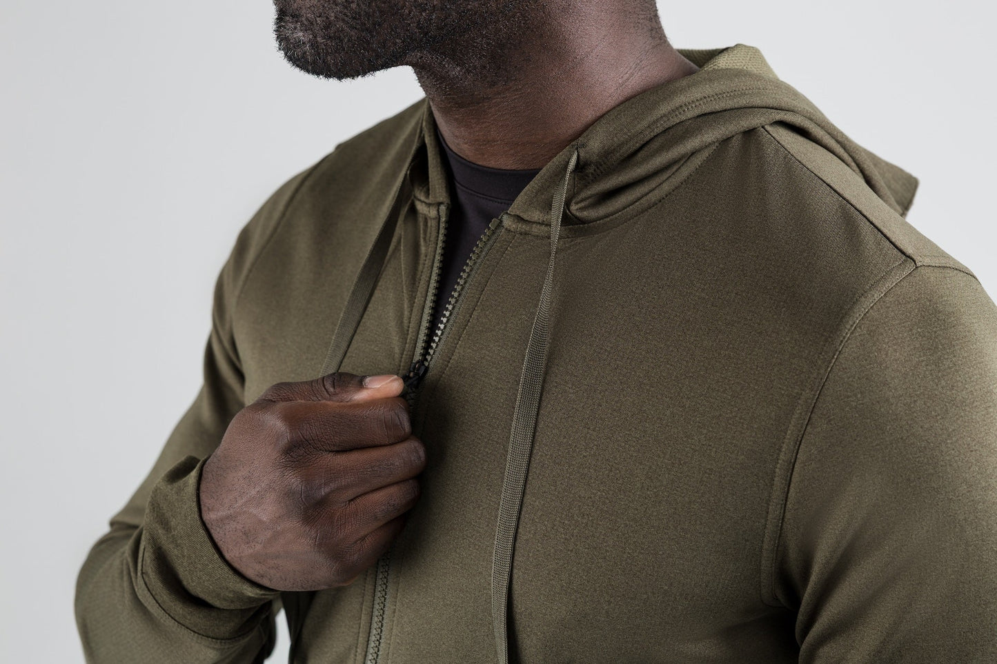 Men's Hoodies and Jackets - Close up of man zipping up the olive Attis Jacket with a gray background.