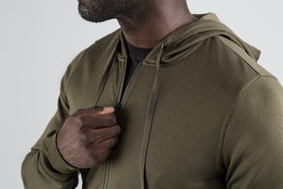 Men's Hoodies and Jackets - Close up of man zipping up the olive Attis Jacket with a gray background.
