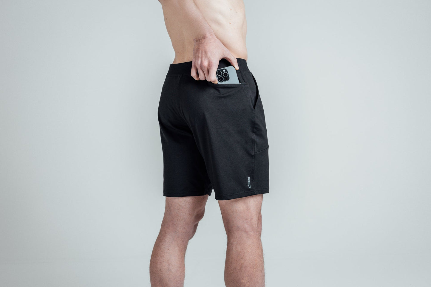 Close-up shot of an athlete putting his phone in the zipper pocket of REP’s Men’s Apollo Shorts