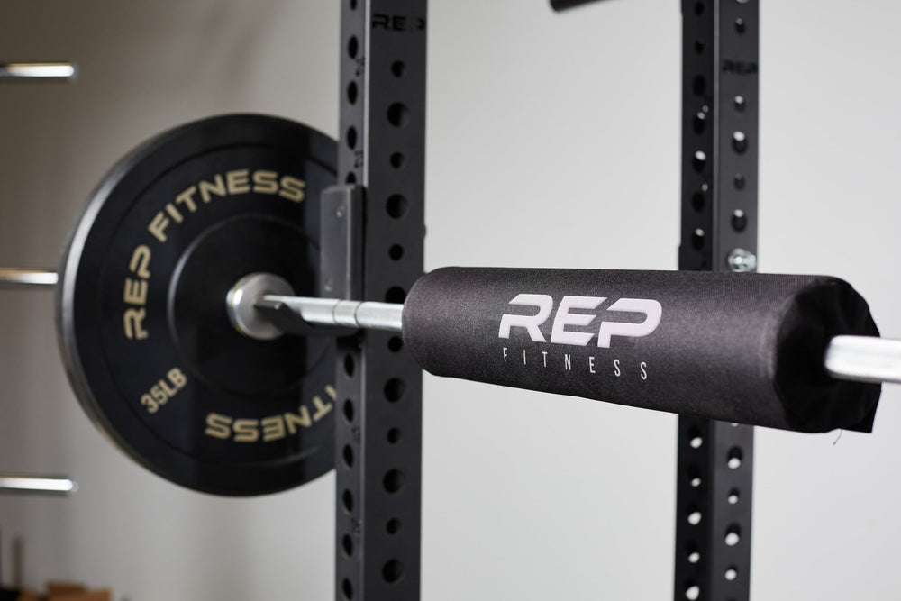 Barbell Shoulder Pad on barbell, soft, durable squat and hip thrust pad with Velcro closure for easy attachment; protects shoulders, neck, and hips during lifts; made from nitrile rubber and Oxford cloth; 17” long, 4” diameter with white REP Fitness logo stitching for comfort and stylefrom Rep Fitness UK | Shop Premium Gym Equipment for Home & Commercial Use, Best Online Gym Equipment UK