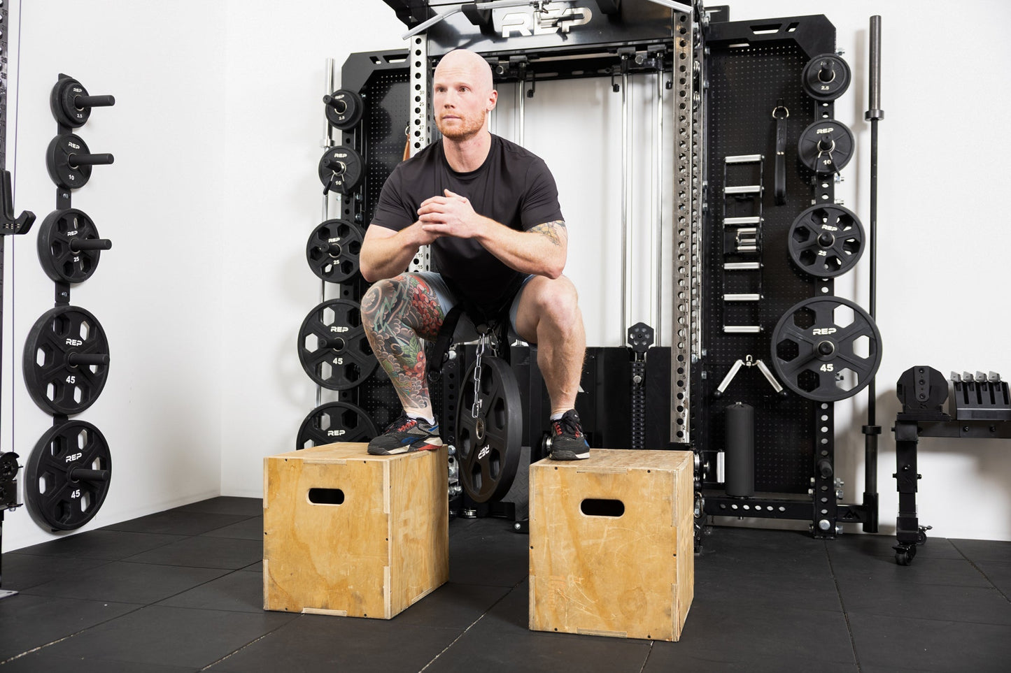 Person using the belt squat belt to do weighted squats. Using two plyo boxes to stand on top of while the weight dangles from the belt in between from Rep Fitness UK | Shop Best Premium Gym Equipment for Home & Commercial Use Online