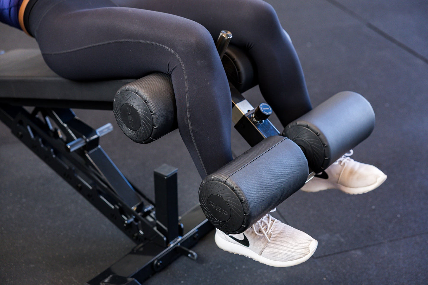 Close-up of an athlete's legs secured in the Adjustable Bench Leg Roller Attachment 2.0 from Rep Fitness UK | Shop Best Premium Gym Equipment for Home & Commercial Use Online