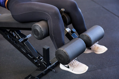 Close-up of an athlete's legs secured in the Adjustable Bench Leg Roller Attachment 2.0 from Rep Fitness UK | Shop Best Premium Gym Equipment for Home & Commercial Use Online