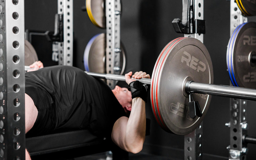 An athlete bench pressing in a PR-5000 rack with Rep Fitness Calibrated Steel Plates (KG) loaded on the barbell from Rep Fitness UK | Shop Best Premium Gym Equipment for Home & Commercial Use Online