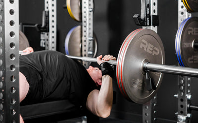 An athlete bench pressing in a PR-5000 rack with Rep Fitness Calibrated Steel Plates (KG) loaded on the barbell from Rep Fitness UK | Shop Best Premium Gym Equipment for Home & Commercial Use Online