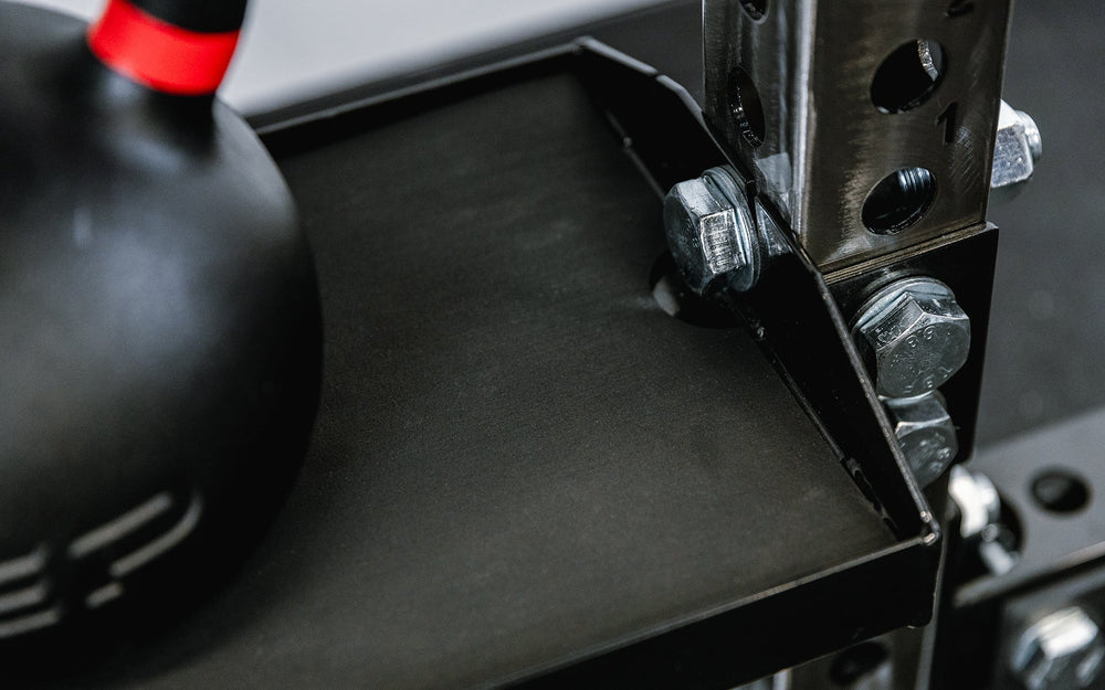 Close-up of metal bracket on Dumbbell and Kettlebell Storage Shelf, heavy-duty 11-gauge reversible gym storage shelf for dumbbells, kettlebells, balls, and accessories; 72” metallic black powder-coated rack with laser-cut REP logo, secure lips, and bolt-on design compatible with 4000 and 5000 Series power racks for organized home or commercial gym storage from Rep Fitness UK | Shop Premium Gym Equipment for Home & Commercial Use, Best Online Gym Equipment UK