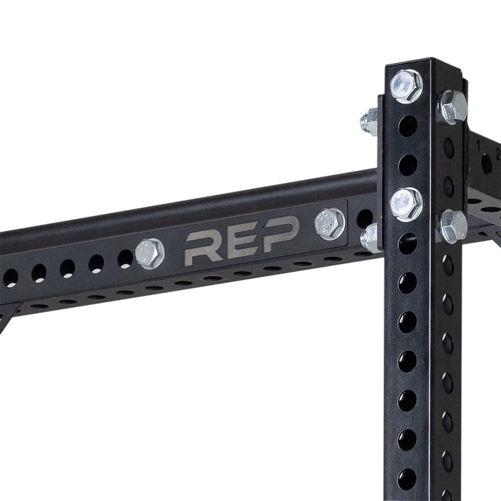 Close Up of Compact Logo Plate Crossmember 5000 Series heavy-duty 3x3” 11-gauge steel rack stabilizer with laser-cut holes, metallic black powder coat, and laser-engraved REP logo from Rep Fitness UK | Shop Premium Gym Equipment for Home & Commercial Use, Best Online Gym Equipment UK