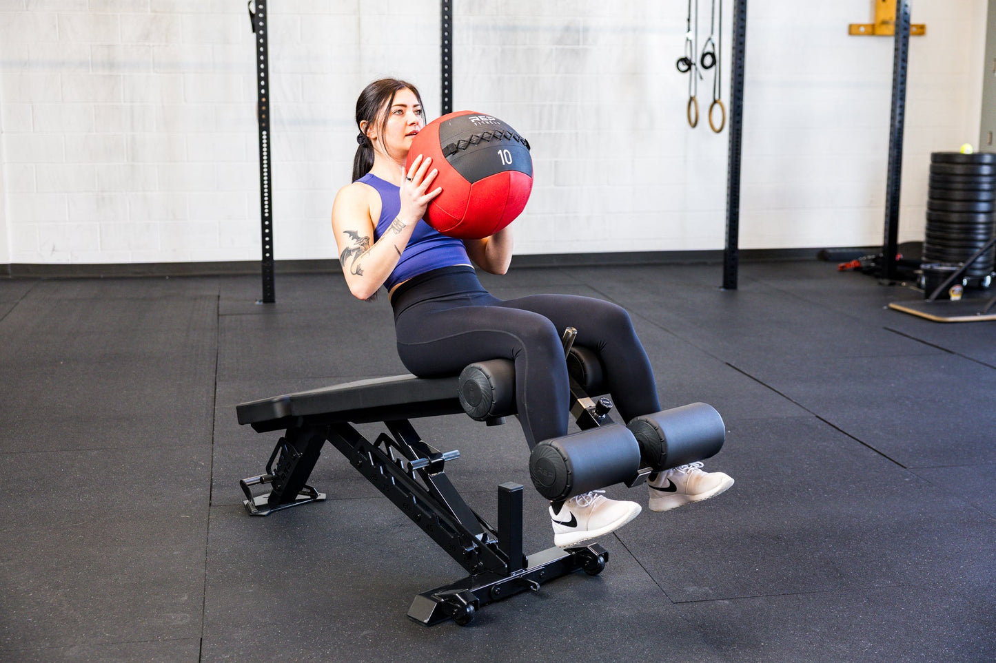 Athlete doing sit ups with the Adjustable Bench Leg Roller Attachment 2.0 and a medicine ball from Rep Fitness UK | Shop Best Premium Gym Equipment for Home & Commercial Use Online