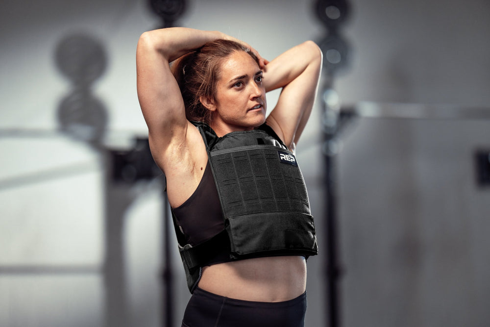 Female Athlete performing upper body stretches in the black Strata Weight Vest, adjustable fit, padded ergonomic design, durable 750D Cordura®, secure plate compartments, and versatile use for strength, HIIT, and functional fitness from Rep Fitness UK | Shop Premium Gym Equipment for Home & Commercial Use, Best Online Gym Equipment UK