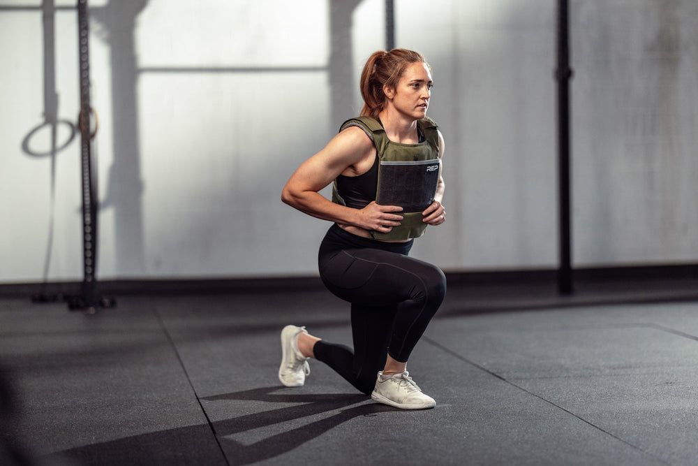 Female Athlete wearing the olive Strata Weight Vest doing lunges, adjustable fit, padded ergonomic design, durable 750D Cordura®, secure plate compartments, and versatile use for strength, HIIT, and functional fitness from Rep Fitness UK | Shop Premium Gym Equipment for Home & Commercial Use, Best Online Gym Equipment UK