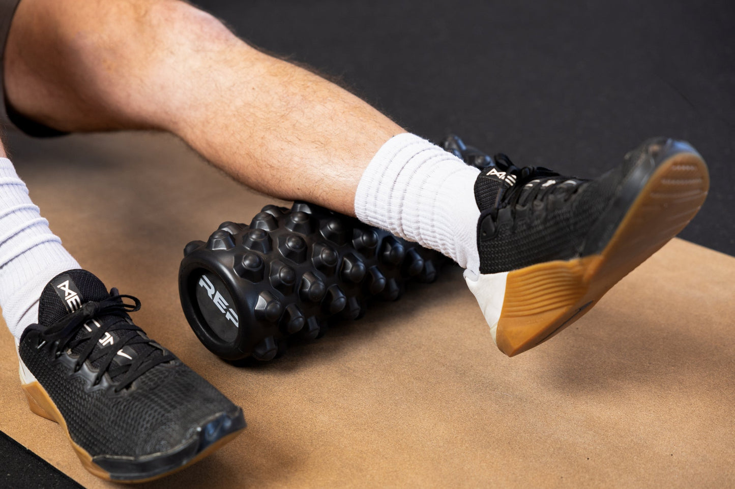 Textured Foam Roller Positioned Under a Person’s Calf for Muscle Recovery from Rep Fitness UK | Shop Best Premium Gym Equipment for Home & Commercial Use Online