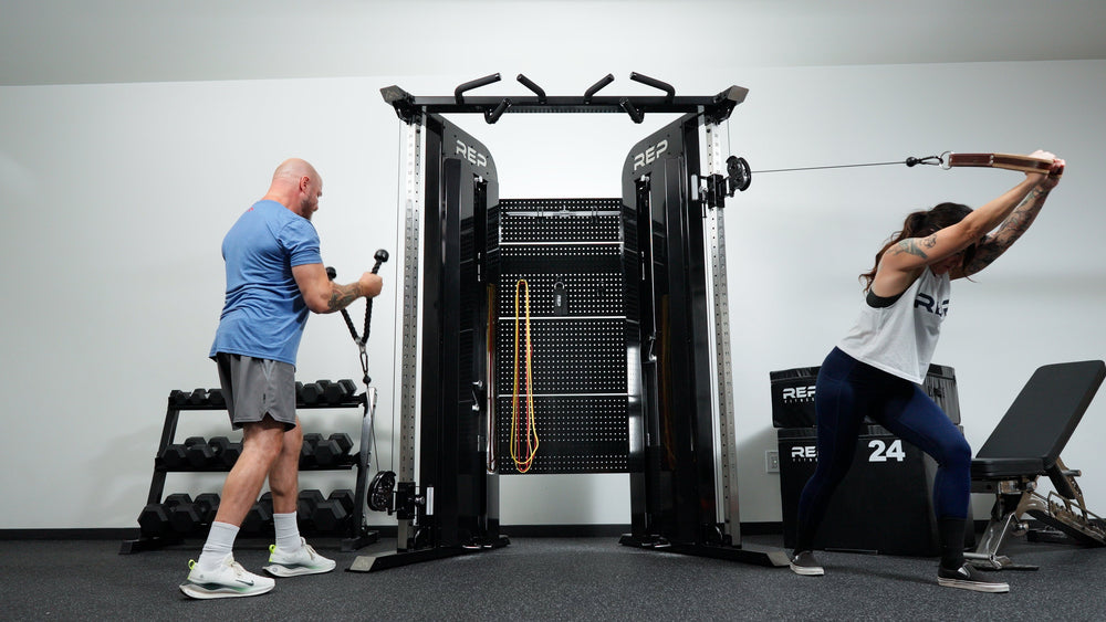 Man and woman simultaneously sitting exercising using pulleys on Arcadia™ max stand-alone functional trainer, premium full-sized cable machine with grips hanging on the back board from Rep Fitness UK | Shop Premium Gym Equipment for Home & Commercial Use Online.