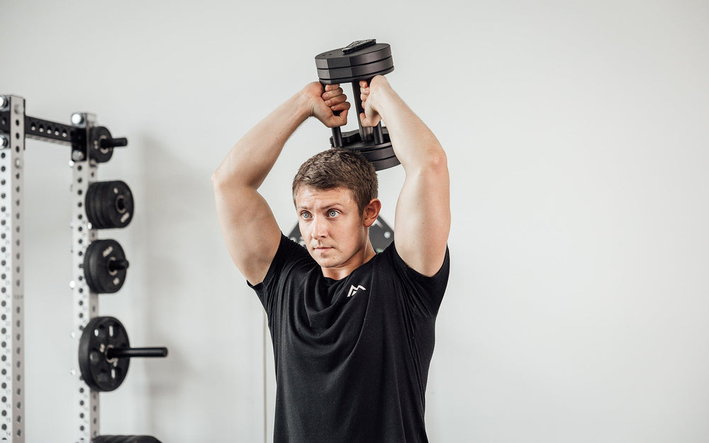 Man doing overhead upper arm and back exercises using Premium QuickDraw dumbbells with adjustable weight, fast switch adjustable  weight range technology and secure Lock-N-Load switches on a storage cart from Rep Fitness UK | Shop Premium Gym Equipment for Home & Commercial Use, Best Online Gym Equipment UK