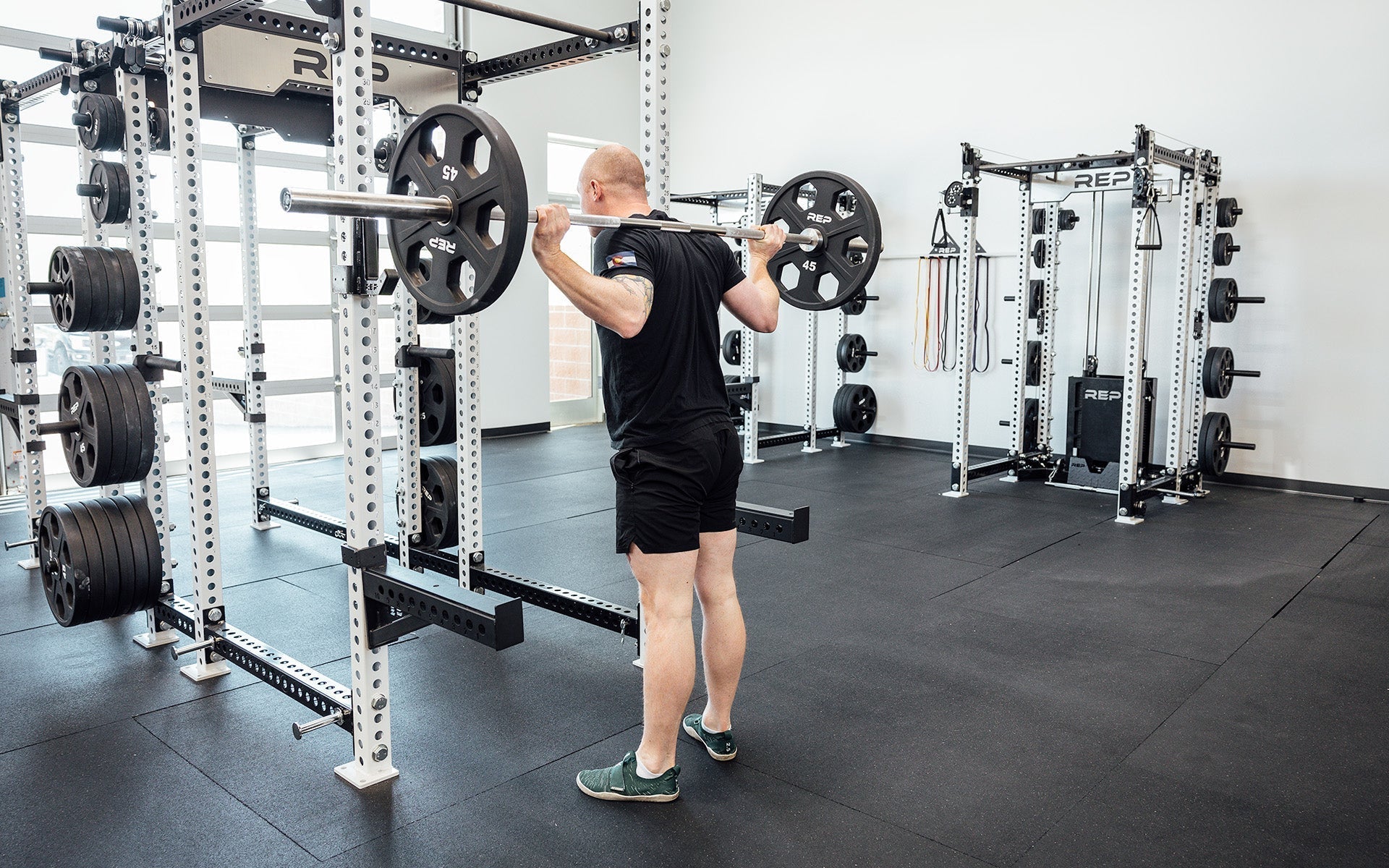 Man doing shoulder lifts with REP Fully Stainless Steel Double Black Diamond Power Bar, elite 20kg powerlifting barbell with ultra-aggressive mountain knurling, 29mm stiff shaft, bronze bushings, and IPF-standard specs, built for maximum grip and durability; available in stainless steel or Cerakote finishes for premium performance and corrosion resistance from Rep Fitness UK | Shop Premium Gym Equipment for Home & Commercial Use, Best UK Gym Equipment Online