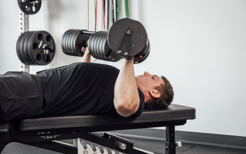 Man lying on weight bench using Premium QuickDraw dumbbells with adjustable weight, fast switch adjustable  weight range technology and secure Lock-N-Load switches on a storage cart from Rep Fitness UK | Shop Premium Gym Equipment for Home & Commercial Use, Best Online Gym Equipment UK