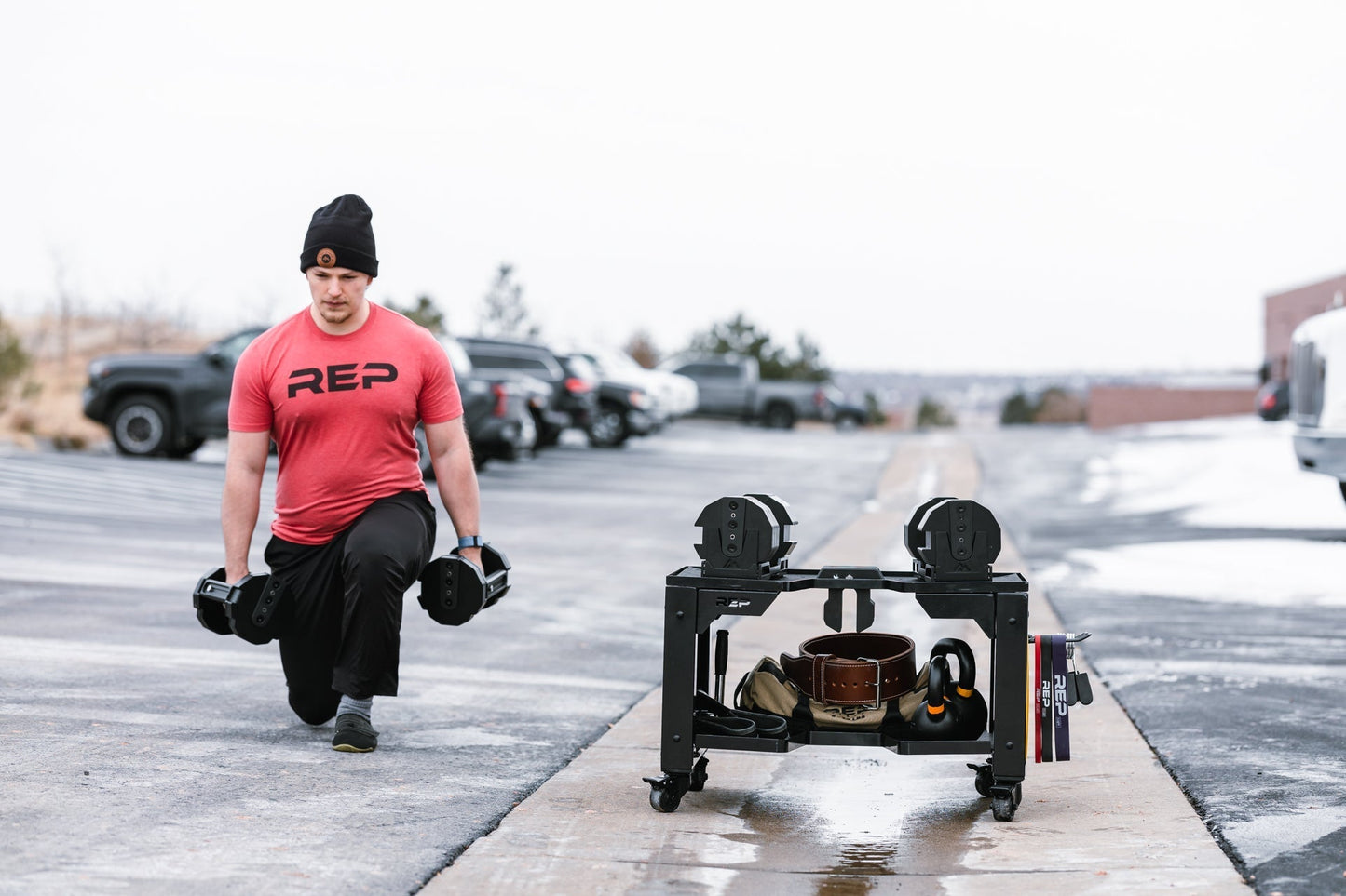 Man outdoors exercising next to premium heavy duty matte black storage cart with wheels in sleek matte black metal finish for organized gym equipment storage loaded with exercise balls, kettlebells and other lifting and exercise equipment from Rep Fitness UK | Shop Premium Gym Equipment for Home & Commercial Use Online