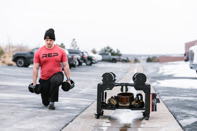 Man outdoors exercising next to premium heavy duty matte black storage cart with wheels in sleek matte black metal finish for organized gym equipment storage loaded with exercise balls, kettlebells and other lifting and exercise equipment from Rep Fitness UK | Shop Premium Gym Equipment for Home & Commercial Use Online