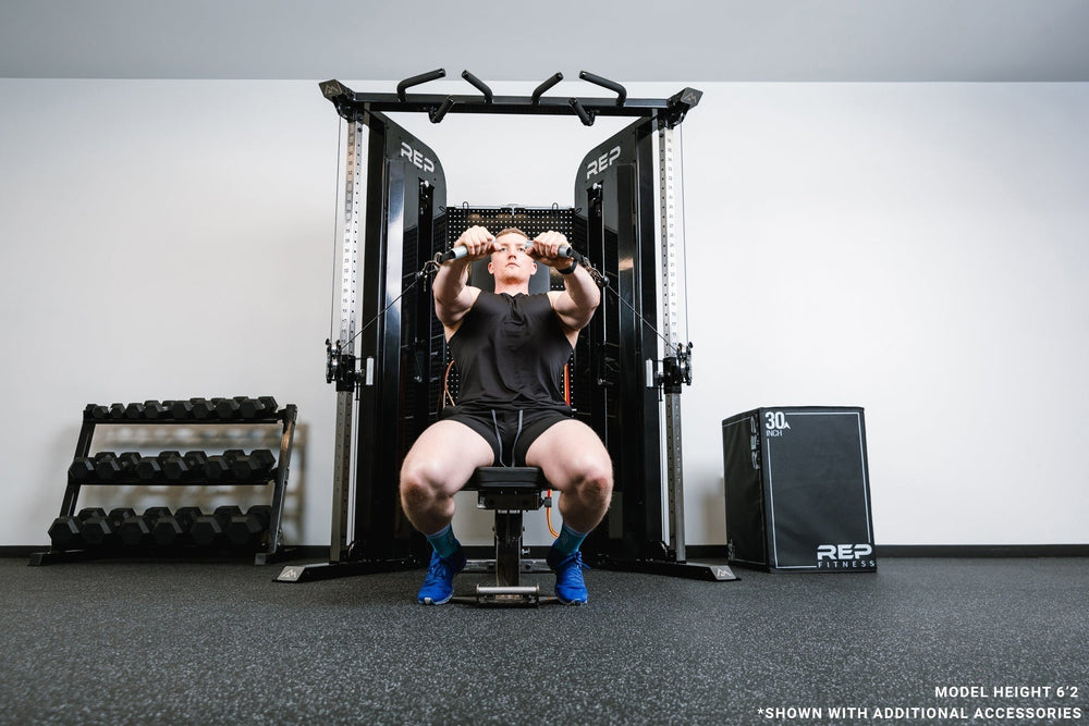 Man sitting on bench using pulleys on Arcadia™ max stand-alone functional trainer, premium full-sized cable machine with grips hanging on the back board from Rep Fitness UK | Shop Premium Gym Equipment for Home & Commercial Use Online.