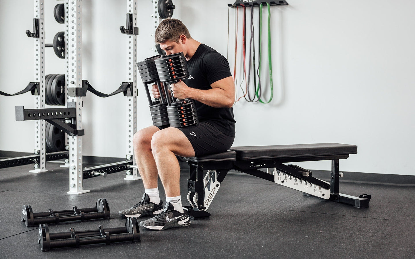 Man sitting up right on weight bench using Premium QuickDraw dumbbells with adjustable weight, fast switch adjustable  weight range technology and secure Lock-N-Load switches on a storage cart from Rep Fitness UK | Shop Premium Gym Equipment for Home & Commercial Use, Best Online Gym Equipment UK