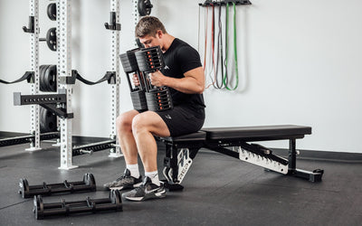 Man sitting up right on weight bench using Premium QuickDraw dumbbells with adjustable weight, fast switch adjustable  weight range technology and secure Lock-N-Load switches on a storage cart from Rep Fitness UK | Shop Premium Gym Equipment for Home & Commercial Use, Best Online Gym Equipment UK
