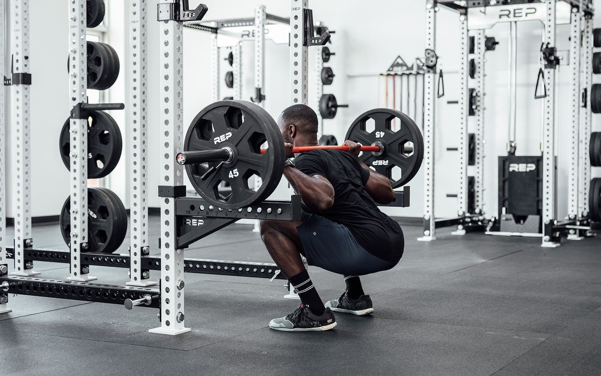Man squatting with 20 kg Colorado weightlifting bar and 90 kgs weights with a red metal finish bar, ideal for strength training and gym workouts from Rep Fitness UK | Shop Premium Gym Equipment for Home & Commercial