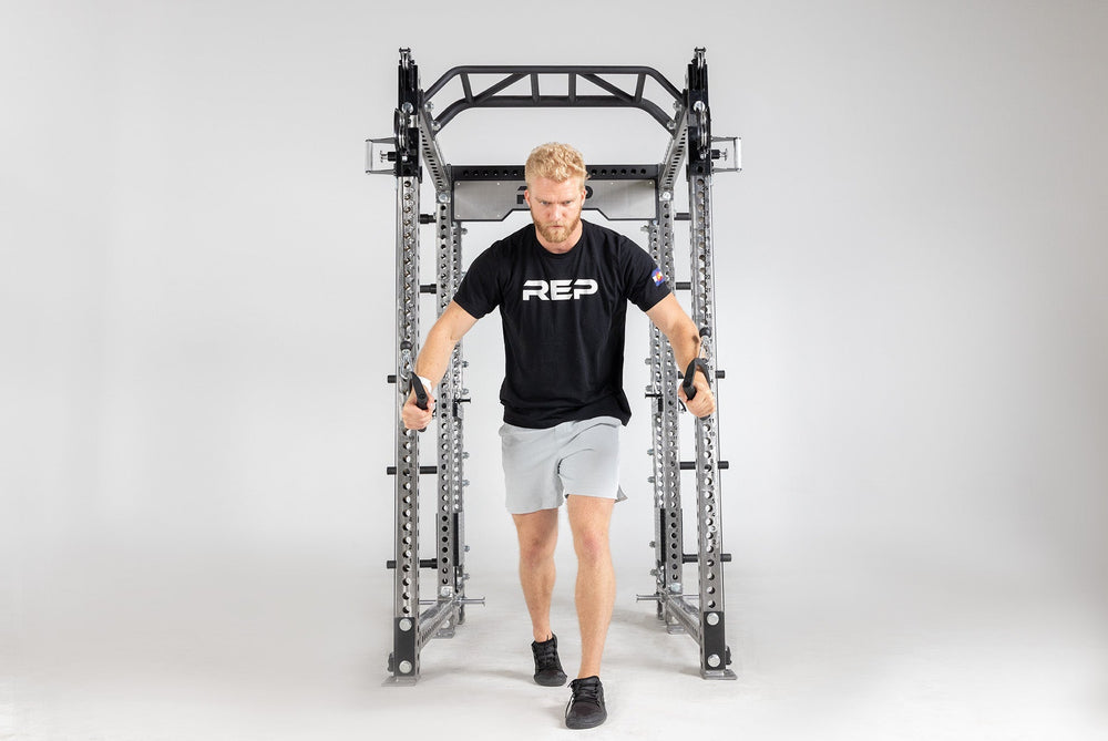 Man using trainer with Logo Plate Crossmember 5000 Series heavy-duty gauge steel rack stabilizer with laser-cut holes, enhances rack stability and adds premium gym aesthetics from Rep Fitness UK | Shop Premium Gym Equipment for Home & Commercial Use, Best Online Gym Equipment UK