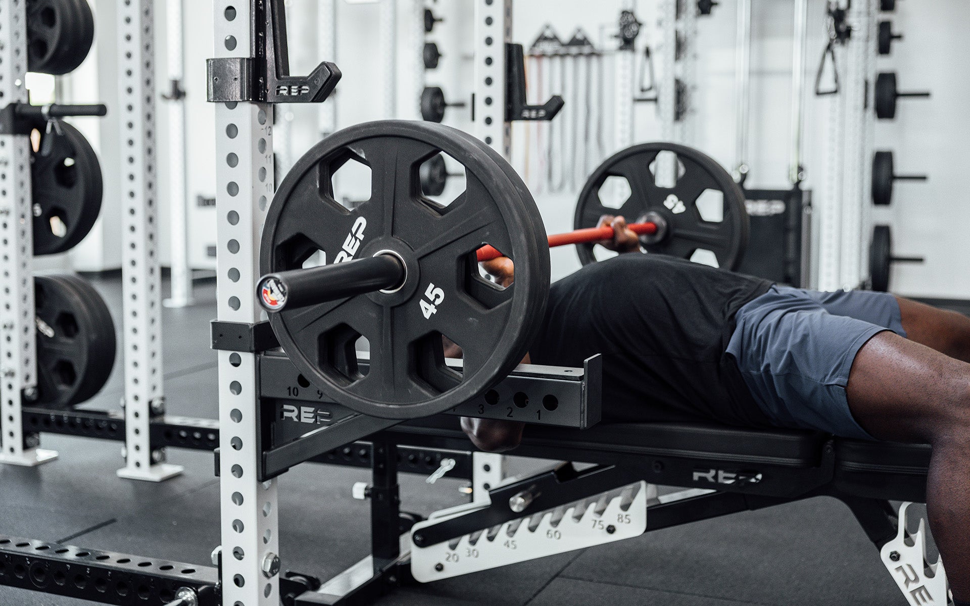 Man working upper body with 20 kg Colorado weightlifting red metal shaft bar and 90 kgs weights with a red metal finish bar, ideal for strength training and gym workouts from Rep Fitness UK | Shop Premium Gym Equipment for Home & Commercial facilities