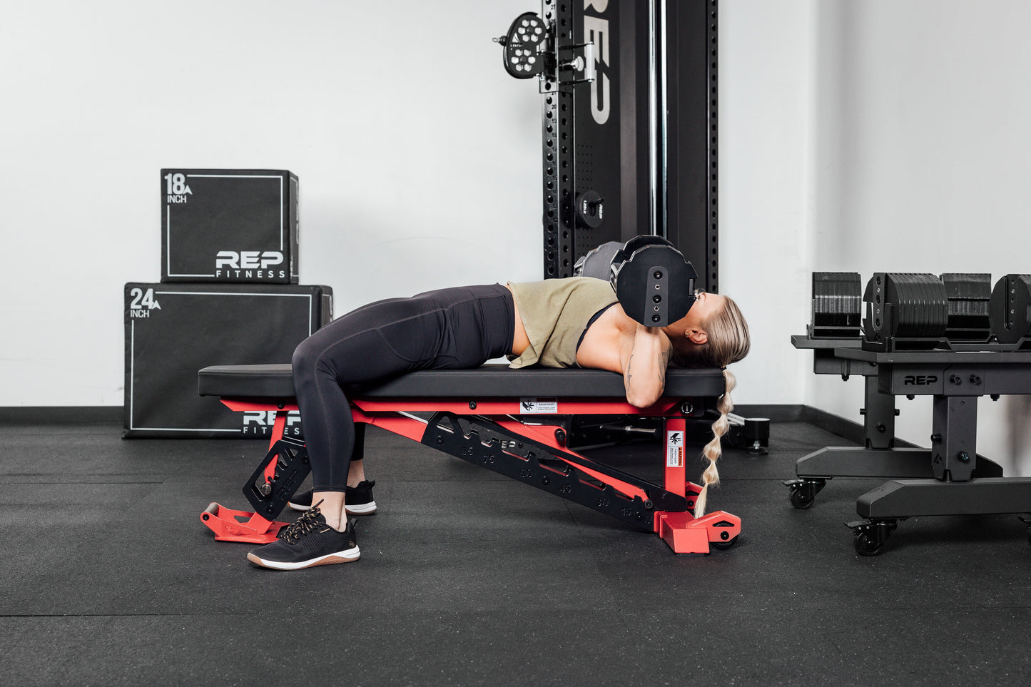 Nighthawk exercise bench red woman using Pepin dumbbells from Rep Fitness UK | Shop Premium Gym Equipment for Home & Commercial Use Online compact, high-performance bench for home and light-commercial gyms; 7- and 14-gauge steel frame, 7 back and 4 seat positions, CleanGrip™ vinyl pad, knurled handle, heavy-duty wheels, IPF-compliant 16.7” height, vertical storage, and compatibility with leg curl and roller attachments from Rep Fitness UK | Shop Best Premium Gym Equipment for Home & Commercial Use Online