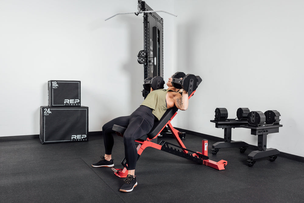 Nighthawk exercise red bench woman laying on using Pepin dumbbells for reps from Rep Fitness UK | Shop Premium Gym Equipment for Home & Commercial Use Online compact, high-performance bench for home and light-commercial gyms; 7- and 14-gauge steel frame, 7 back and 4 seat positions, CleanGrip™ vinyl pad, knurled handle, heavy-duty wheels, IPF-compliant 16.7” height, vertical storage, and compatibility with leg curl and roller attachments from Rep Fitness UK | Shop Best Premium Gym Equipment for Home & Comme