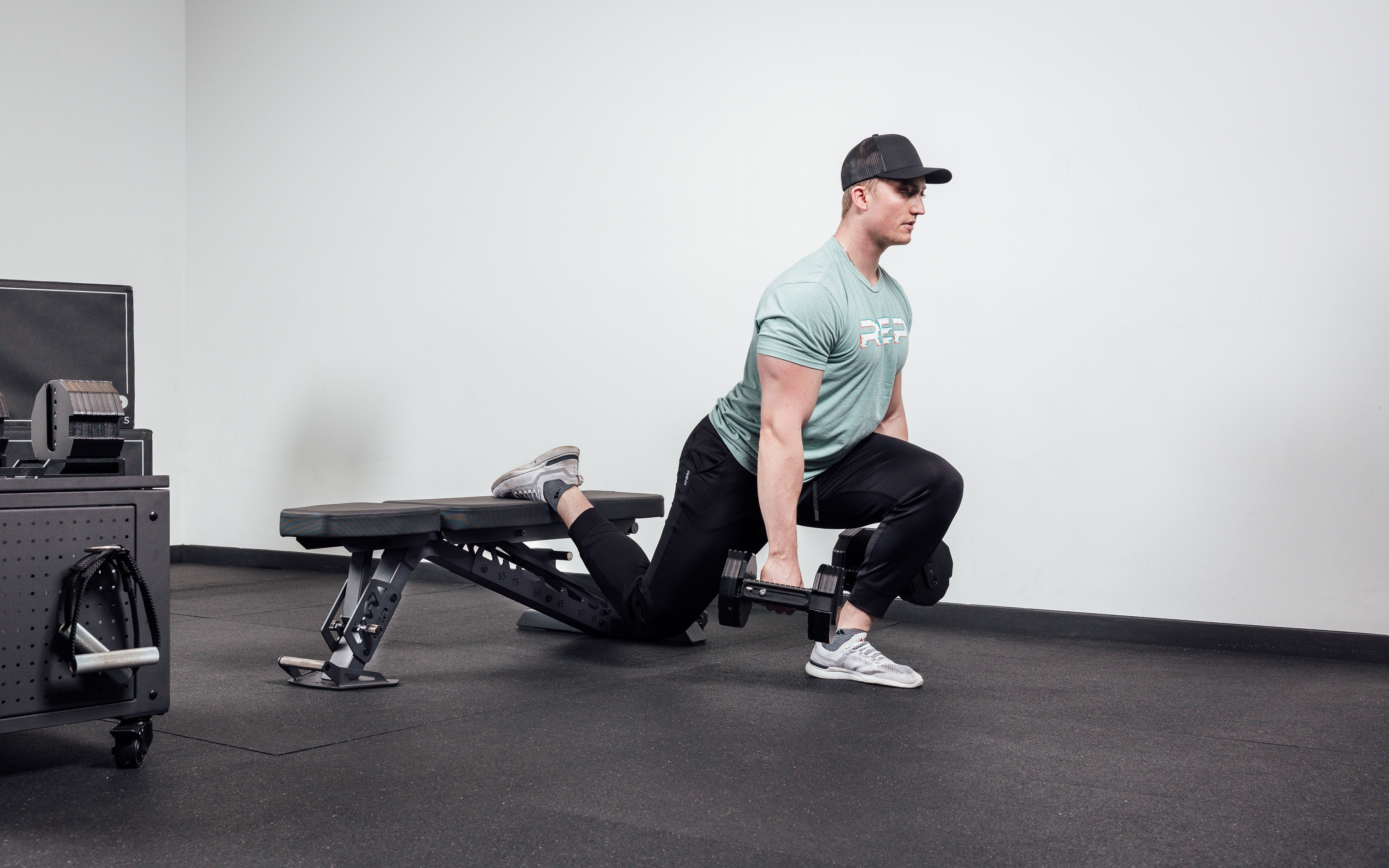Nighthawk matte black bench man exercising legs holding Pepin dumbbells for reps from Rep Fitness UK | Shop Premium Gym Equipment for Home & Commercial Use Online