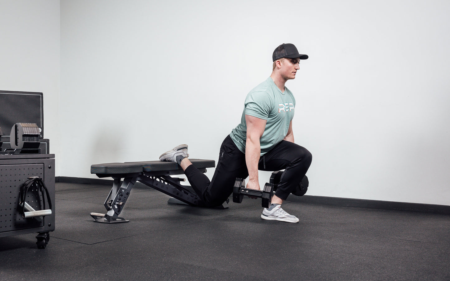 Nighthawk matte black bench man exercising legs holding Pepin dumbbells for reps from Rep Fitness UK | Shop Premium Gym Equipment for Home & Commercial Use Online