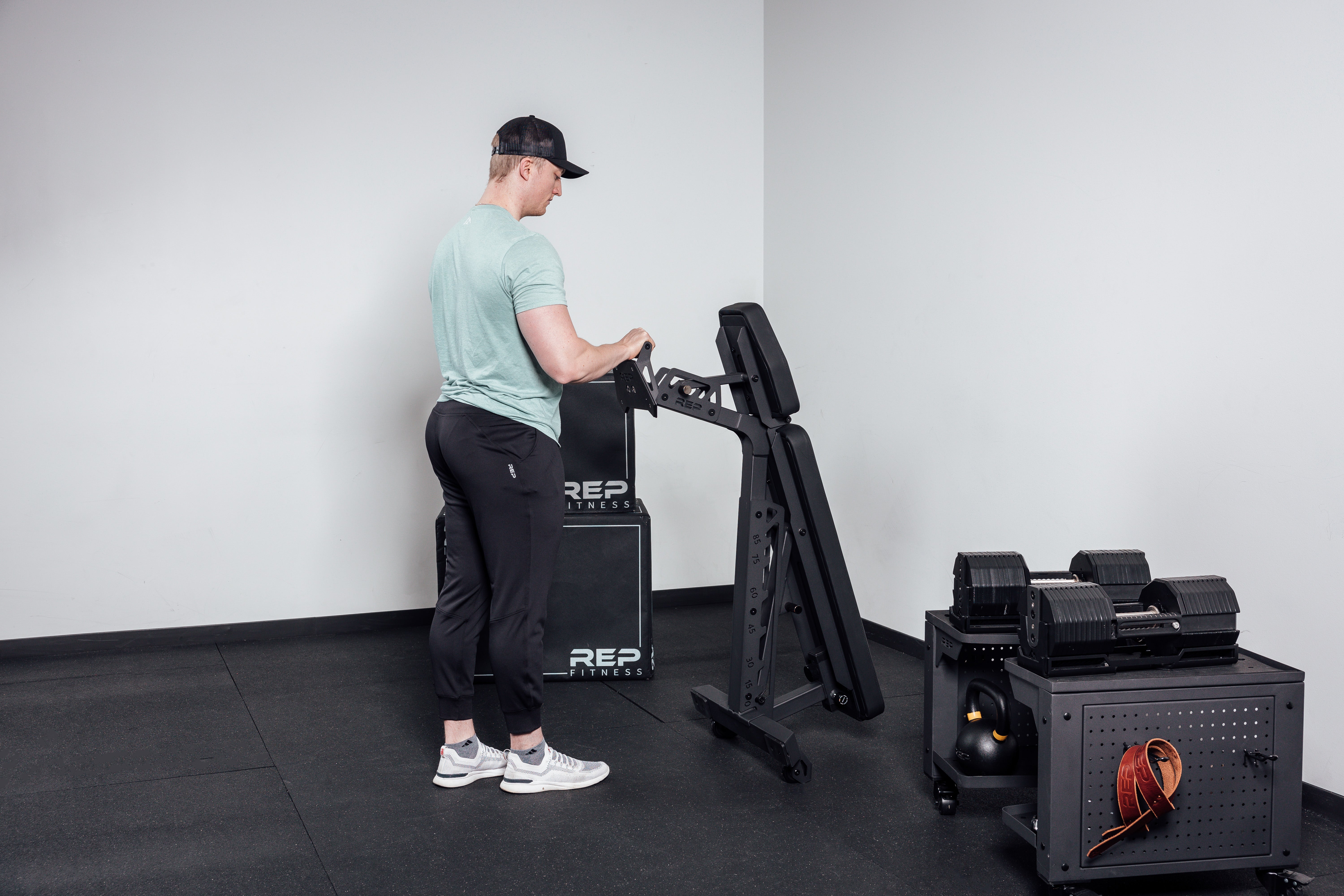 Nighthawk matte black bench man rolling folded bench into corner for tidy storage from Rep Fitness UK | Shop Premium Gym Equipment for Home & Commercial Use Online