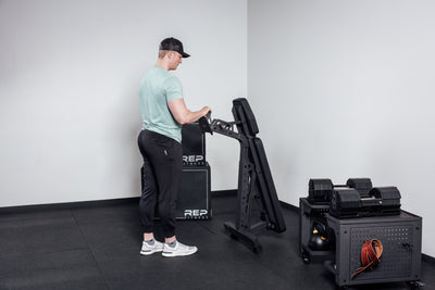 Nighthawk matte black bench man rolling folded bench into corner for tidy storage from Rep Fitness UK | Shop Premium Gym Equipment for Home & Commercial Use Online