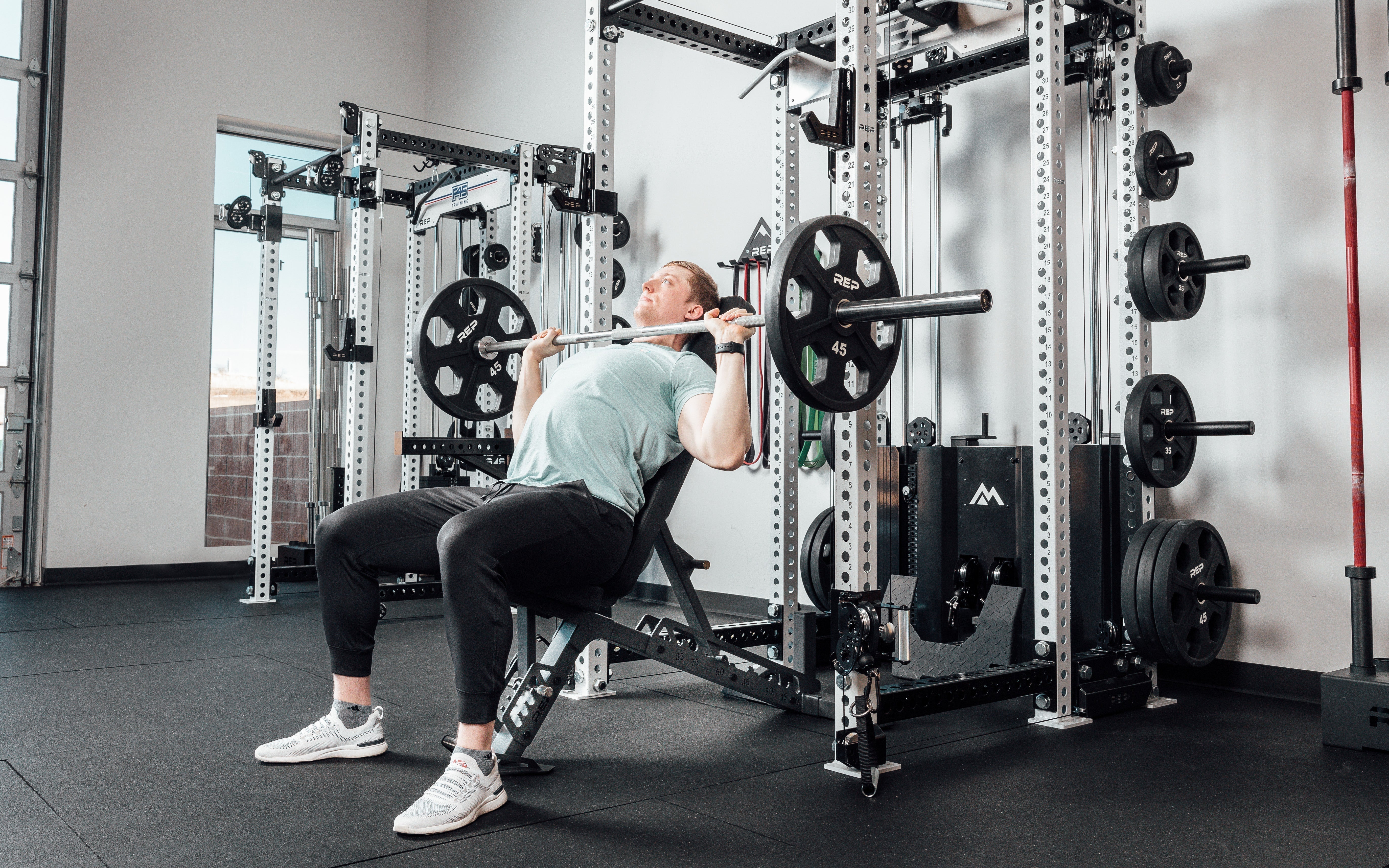 Nighthawk matte black bench man sitting using weights for reps from Rep Fitness UK | Shop Premium Gym Equipment for Home & Commercial Use Online