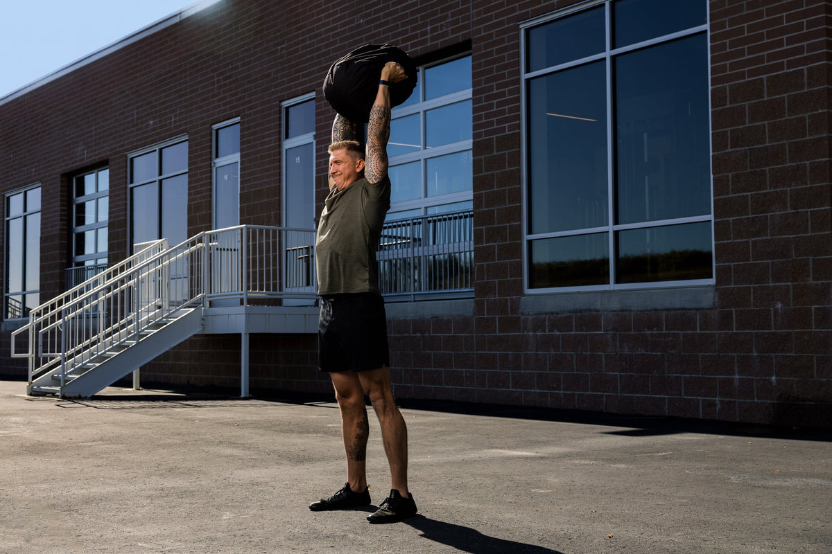 Man doing a stone sandbag press overhead.