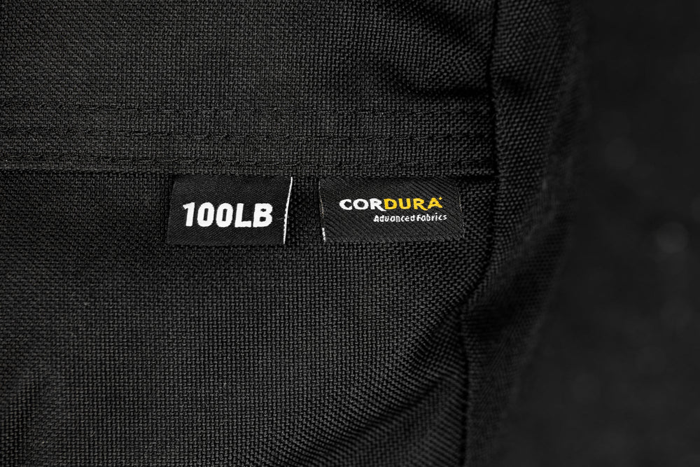 Close-up of a black fabric with '100LB' and 'Cordura' labels on a dark background

