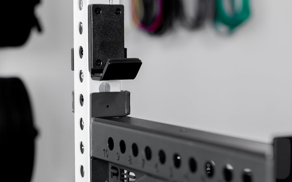 Side view of standard J-Cups 2.0 – heavy-duty barbell holder for PR-5000 power rack; 3x3” 11-gauge steel with metallic black powder coat, soft plastic lining, recessed hardware, and 1,000 lb capacity for safe, scratch-free, and stable lifting mounted on white power rack upright  from Rep Fitness UK | Shop Premium Gym Equipment for Home & Commercial Use, Best Online Gym Equipment UK