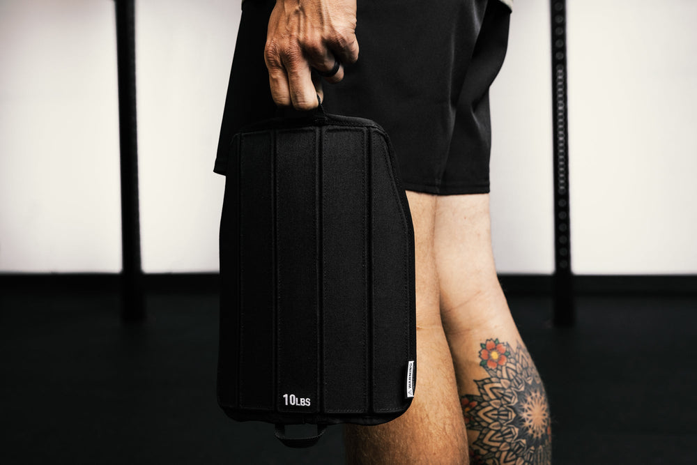 Person holding a black soft weight vest plate with '10 Deep' branding against a neutral background