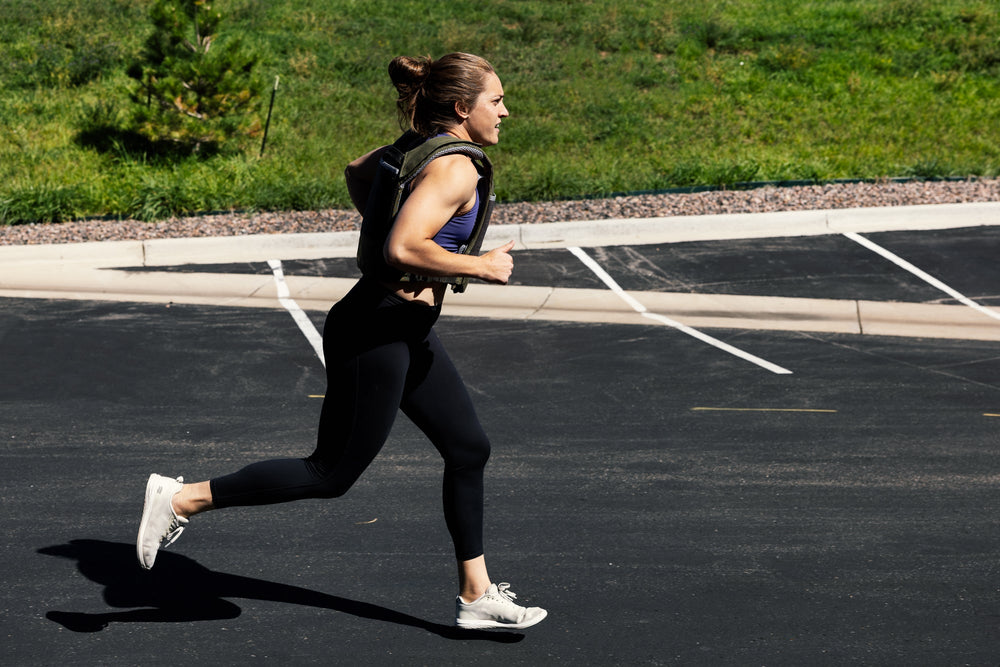 Woman running on a paved road with grass and a tree in the background. wearing weight vest with soft weight vest plates inside