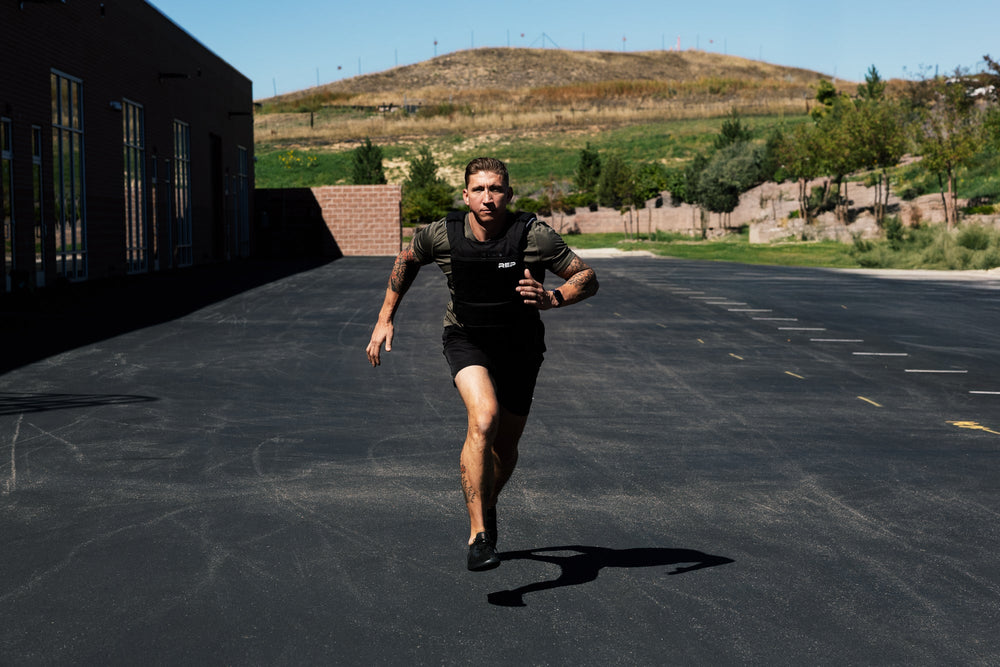 Person running with weight vest and soft weight vest plates inserted . on a paved area with a building and greenery in the background