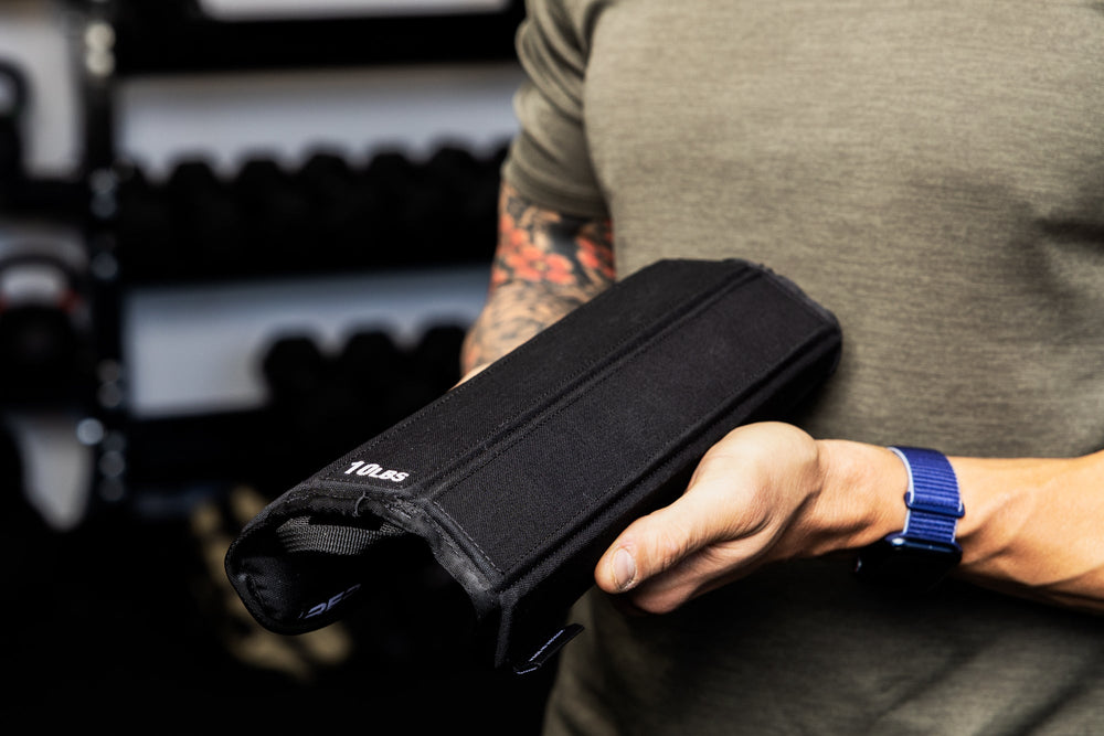 Person holding and showing flexibility of a soft weight vest plate with a visible brand logo in an indoor setting.