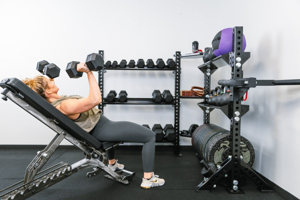 Woman exercising on bench with dumbbells in front of Dumbbell Storage Shelf – heavy-duty 11-gauge steel dumbbell rack shelf with 600lb capacity, metallic black powder-coat finish, laser-cut REP logo, compatible with 4000 and 5000 Series racks, fits full 5–50lb dumbbell sets for organized, space-saving gym storage from Rep Fitness UK | Shop Premium Gym Equipment for Home & Commercial Use, Best Online Gym Equipment UK