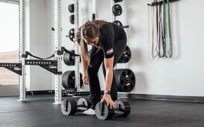 Woman picking up Premium QuickDraw dumbbells with adjustable weight, fast switch adjustable  weight range technology and secure Lock-N-Load switches for high-performance strength training from Rep Fitness UK | Shop Premium Gym Equipment for Home & Commercial Use, Best Online Gym Equipment UK