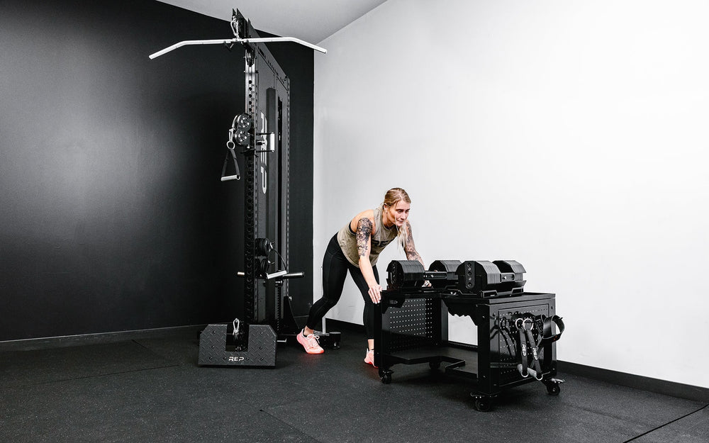 Woman pushing durable matte black storage cart rack with wheels in sleek matte black metal finish for organized gym equipment storage from Rep Fitness UK | Shop Premium Gym Equipment for Home & Commercial Use Online