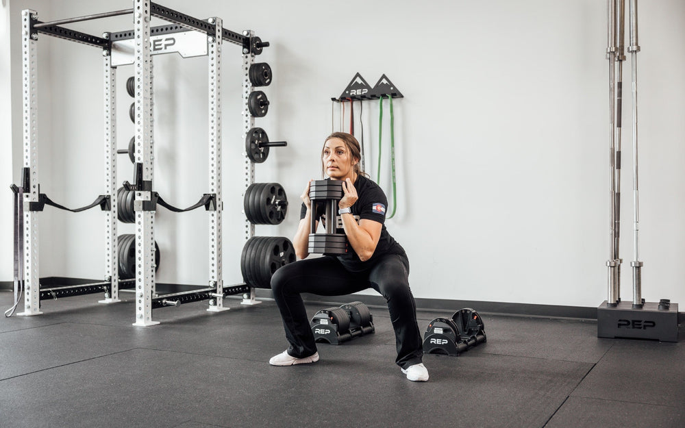 Woman squatting using Premium QuickDraw dumbbells with adjustable weight, fast switch adjustable  weight range technology and secure Lock-N-Load switches for high-performance strength training from Rep Fitness UK | Shop Premium Gym Equipment for Home & Commercial Use, Best Online Gym Equipment UK