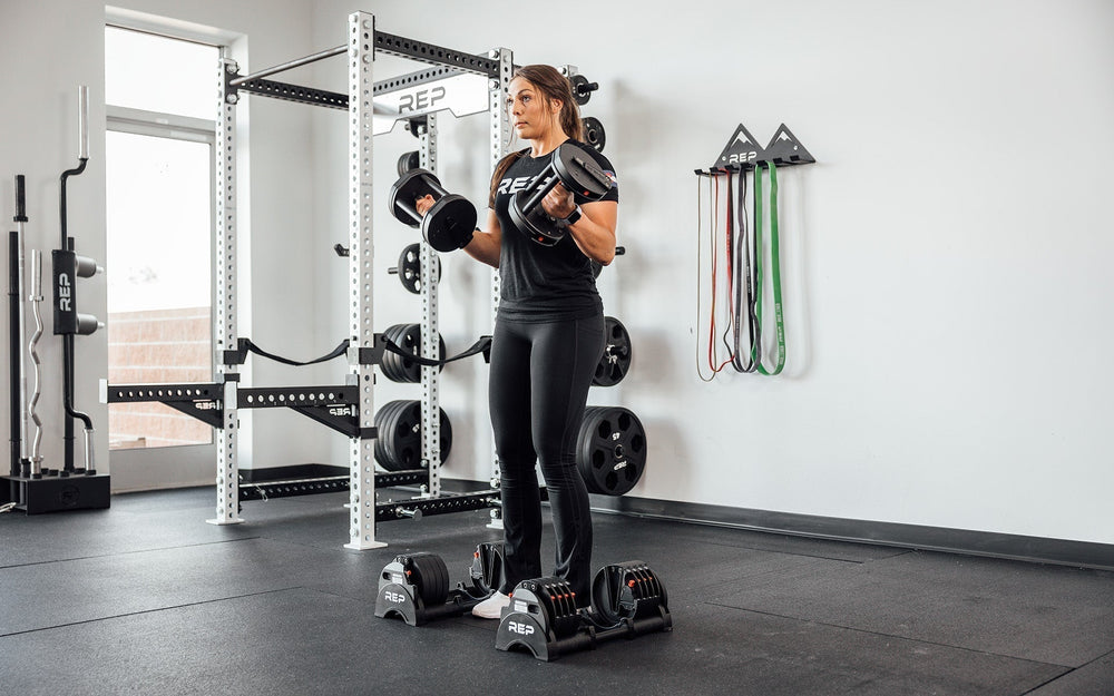 Woman standing doing upper bicep exercises with Premium QuickDraw dumbbells with adjustable weight, fast switch adjustable  weight range technology and secure Lock-N-Load switches for high-performance strength training from Rep Fitness UK | Shop Premium Gym Equipment for Home & Commercial Use, Best Online Gym Equipment UK