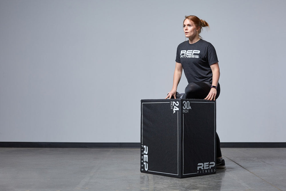 Woman stretching using 30" 3-in-1 Soft Plyo Box showing inside material for safe plyometric training featuring a wood-core interior, impact-absorbing foam, non-slip textured vinyl, and clearly labeled height option for box jumps in home or garage gyms from Rep Fitness UK | Shop Premium Gym Equipment for Home & Commercial Use