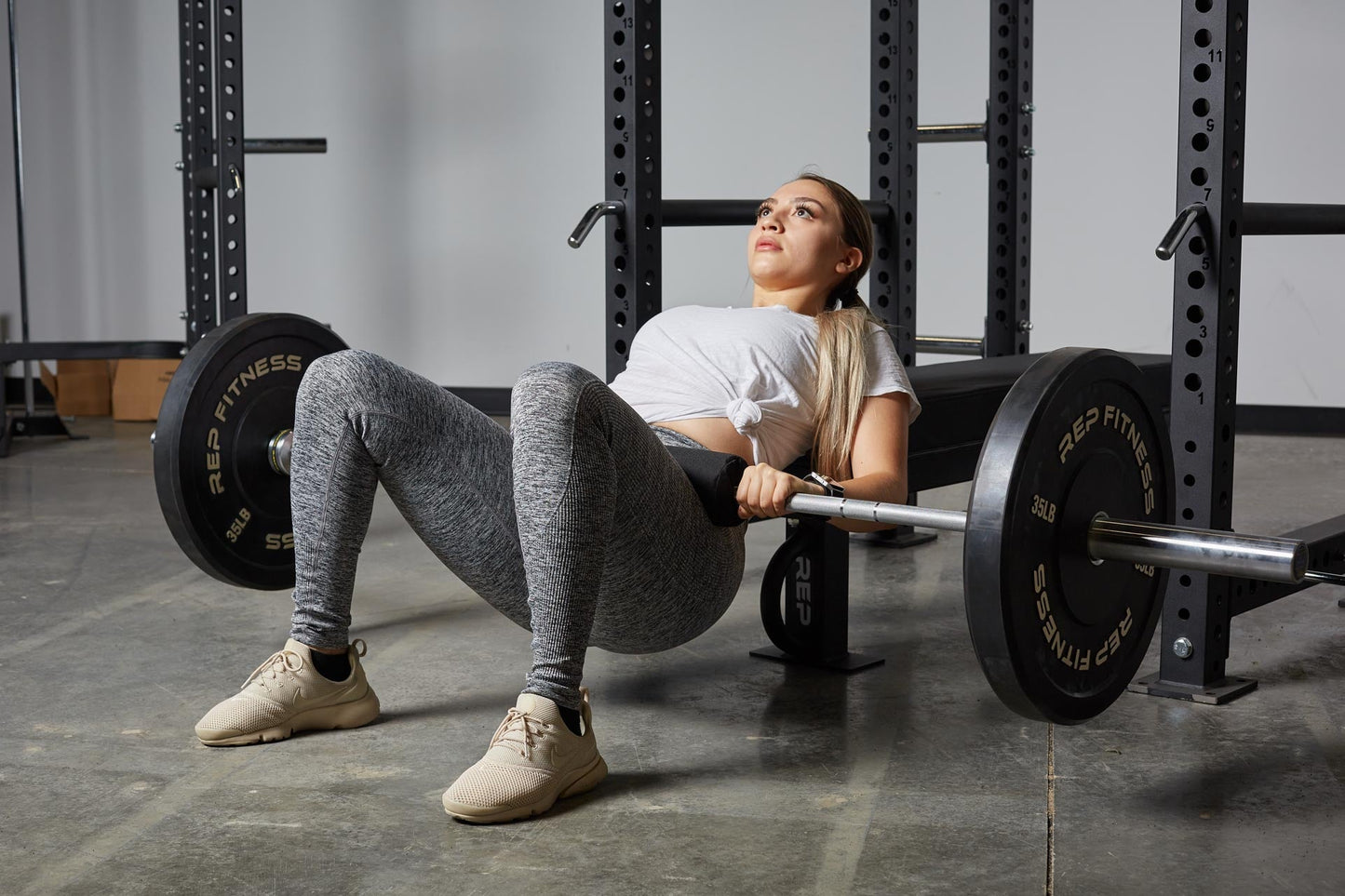 Woman using Barbell Shoulder Pad for glute and stomach reps, soft, durable squat and hip thrust pad with Velcro closure for easy attachment; protects shoulders, neck, and hips during lifts; made from nitrile rubber and Oxford cloth; 17” long, 4” diameter with white REP Fitness logo stitching for comfort and stylefrom Rep Fitness UK | Shop Premium Gym Equipment for Home & Commercial Use, Best Online Gym Equipment UK