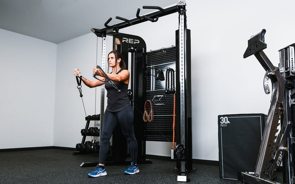 Woman using pulleys on Arcadia™ max stand-alone functional trainer, premium full-sized cable machine with grips hanging on the back board from Rep Fitness UK | Shop Premium Gym Equipment for Home & Commercial Use Online.